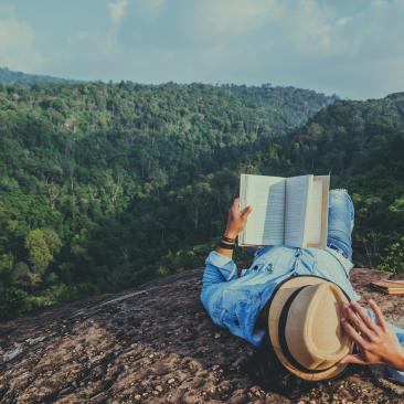 Hombre tumbado leyendo en un bosque